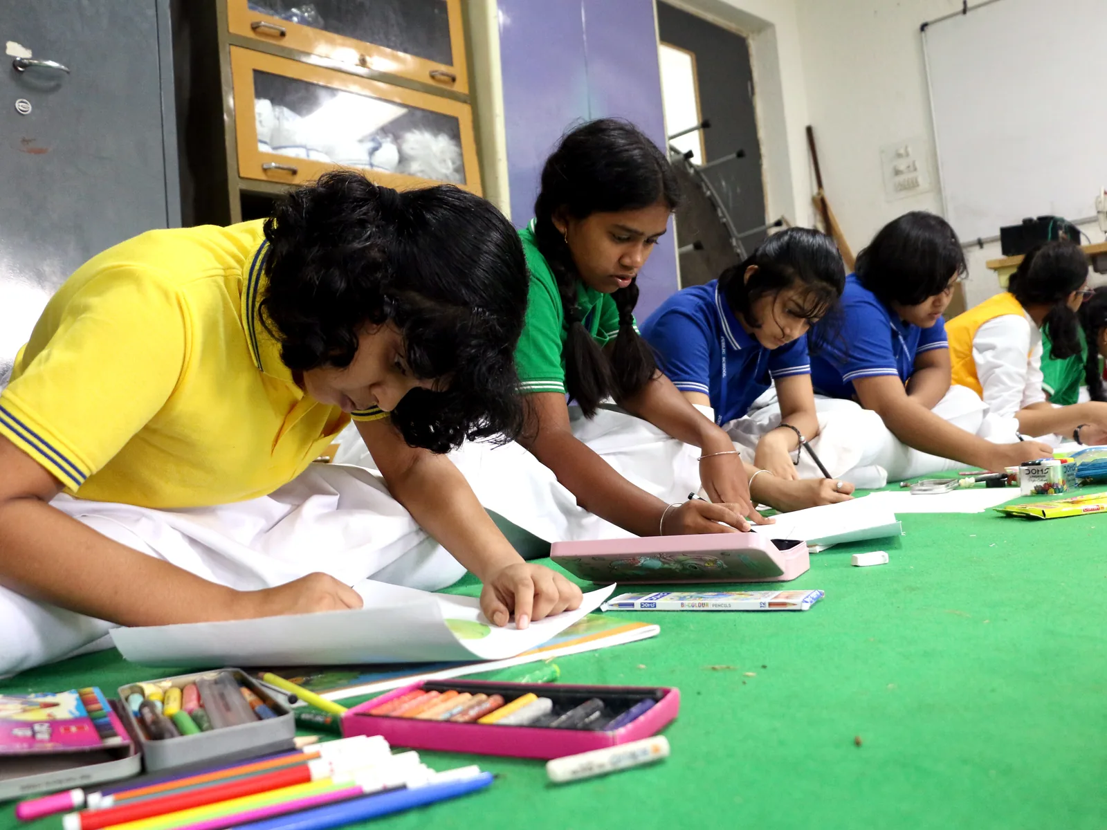 Art students painting on the floor with paints and brushes.