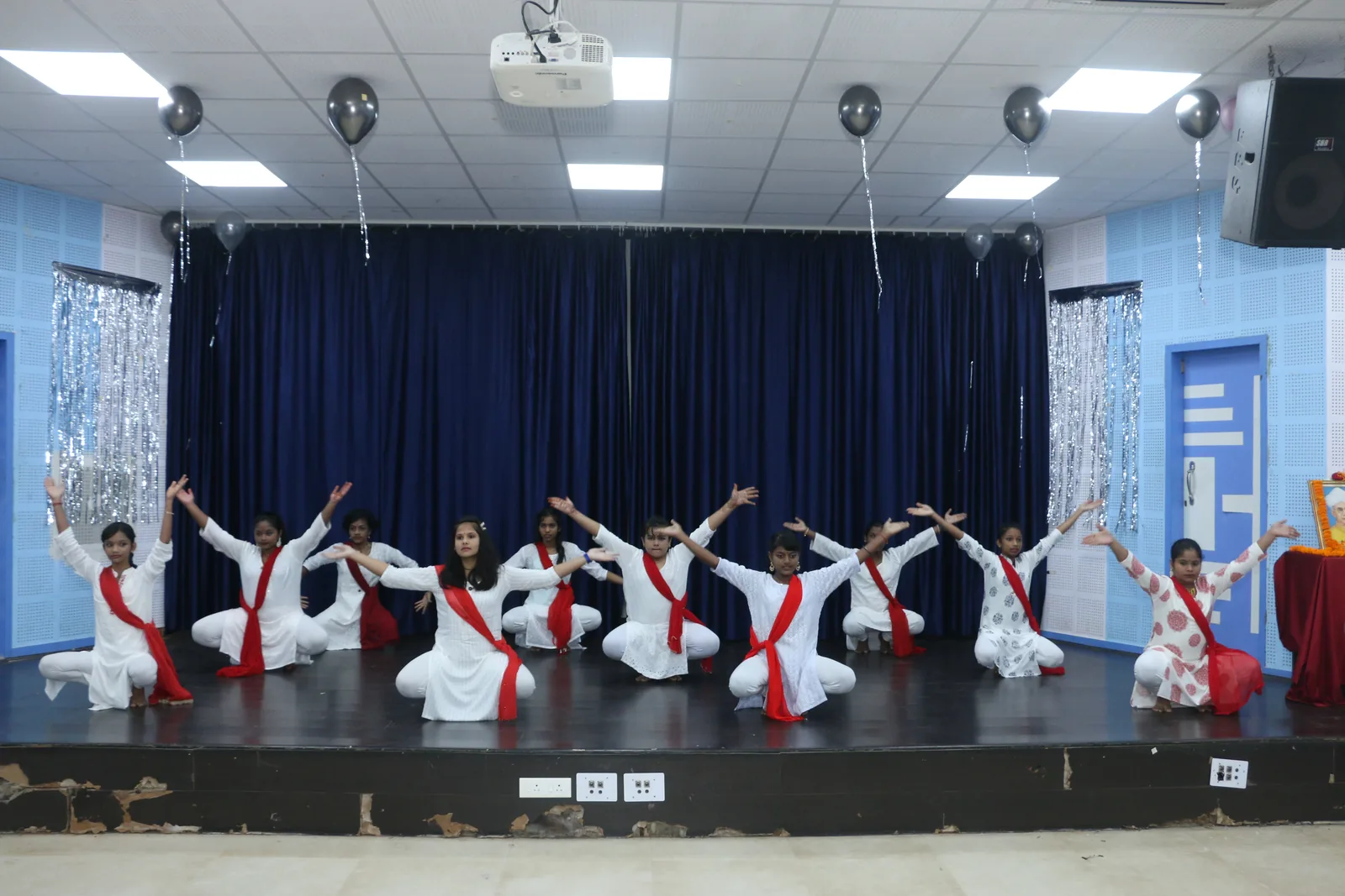 Students performing stage choreography in red and white festive attire.