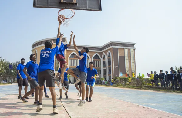 Students jumping for a rebound at the basketball hoop in JPS jerseys.