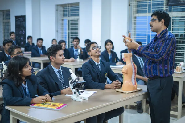 A teacher demonstrating an anatomy model to students with microscopes at their desks.