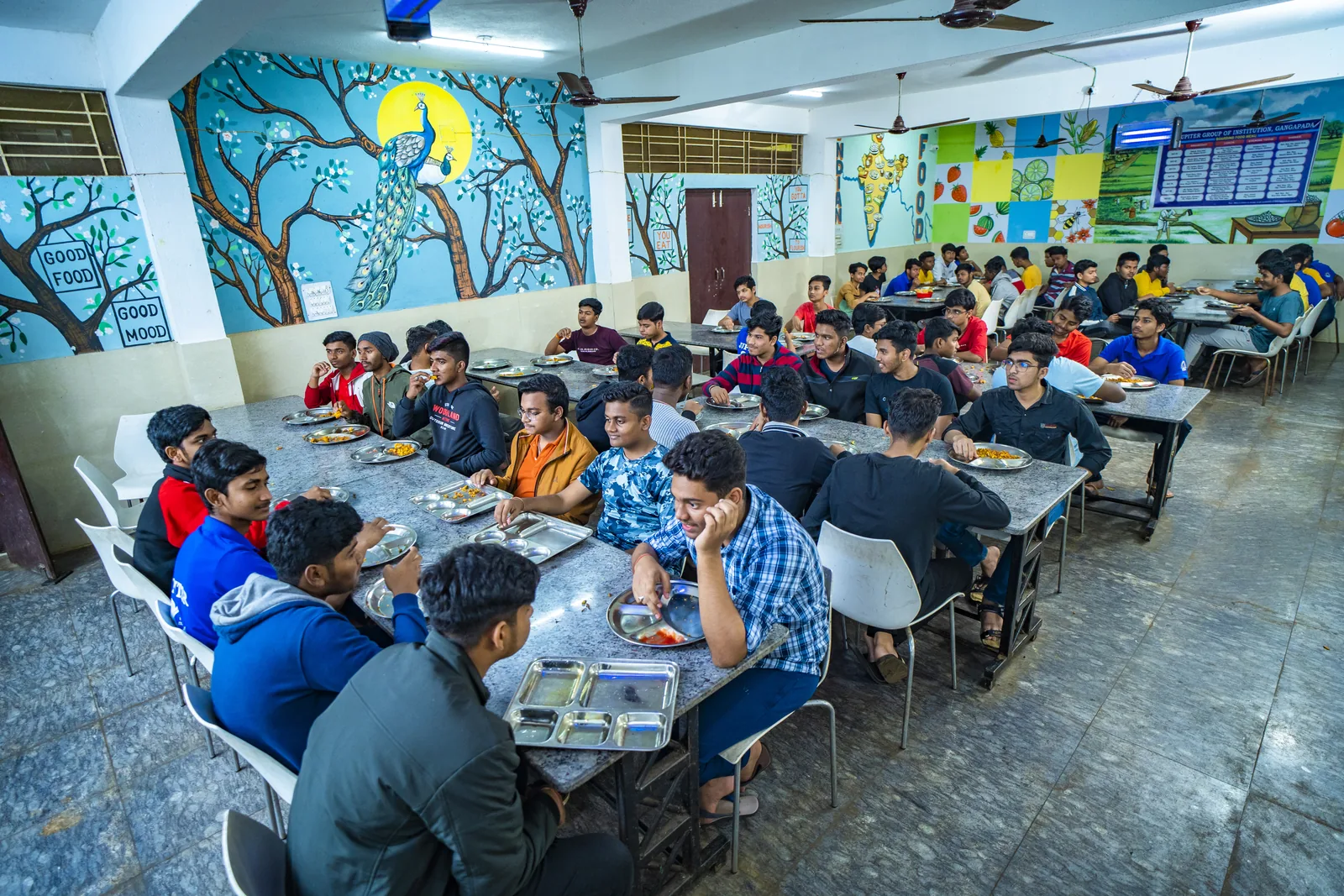 Clean, spacious residential dining hall with banquet tables and peacock mural.