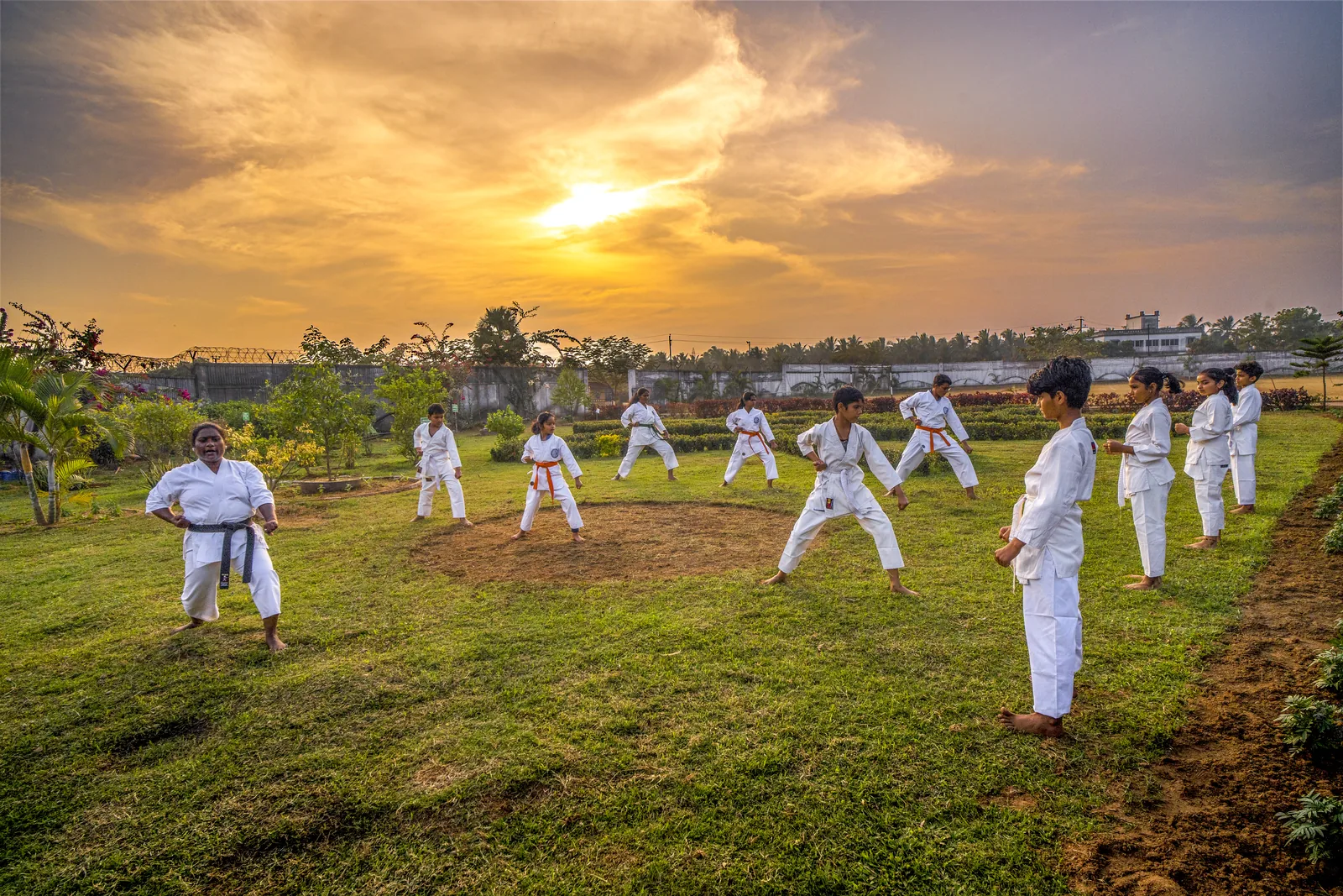 Students in white karate uniforms practicing martial arts on the campus lawn.